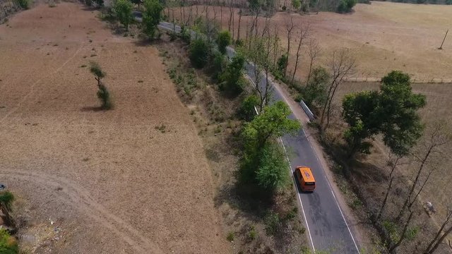A dolly, aerial view of an orange truck driving on a narrow road during the day.
