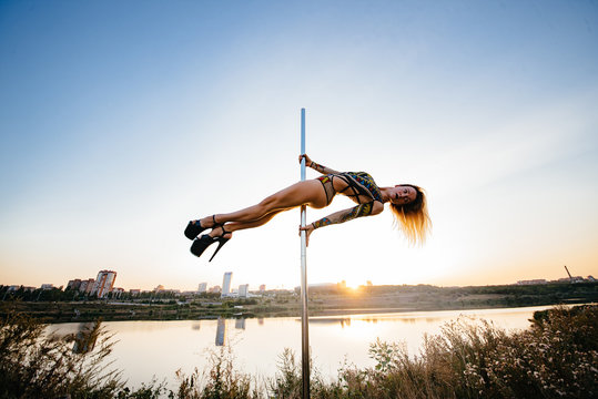 Contrast silhouette photos at sunset against the sky: girl poledancer performs an element on the pole with the split