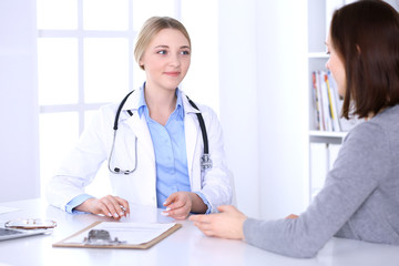 Fototapeta na wymiar Young woman doctor and patient at medical examination at hospital office. Blue color blouse of therapist looks good. Medicine and healthcare concept