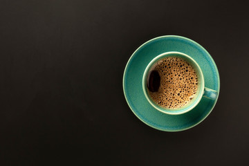 A cup of coffee on a black background, shot from above with copy space