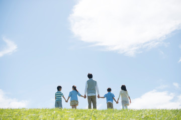 Fototapeta premium 草原で手をつなぐ小学生と先生の後姿