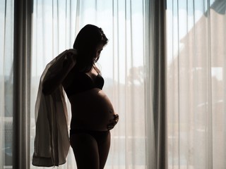 Pregnant woman standing by the window.