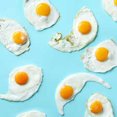 Fried eggs or scrambled eggs pattern on blue background. Creative food concept. Top view. Square crop