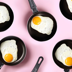 Creative food pattern with fried eggs on pans over pink background. Top view. Creative pattern in minimal style. Flat lay. Square crop