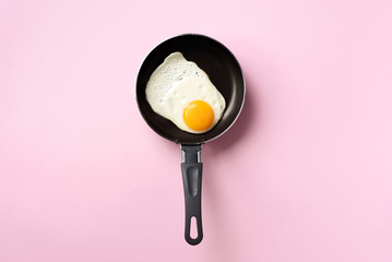 Creative food concept with fried egg on pan over pink background. Top view. Creative pattern in...