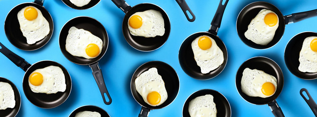 Creative food pattern with fried eggs on pans over blue background. Top view. Creative pattern in minimal style. Flat lay. Banner