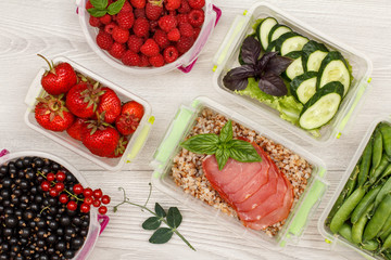 Plastic meal prep containers with boiled buckwheat porridge and slices of meat, fresh cucumbers, salad and berries.