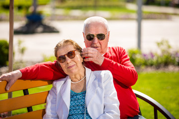 Cheerful senior couple having good time in city park, walking, laughing and enjoying sunny day. Old people wearing color clothes ans sunglasses