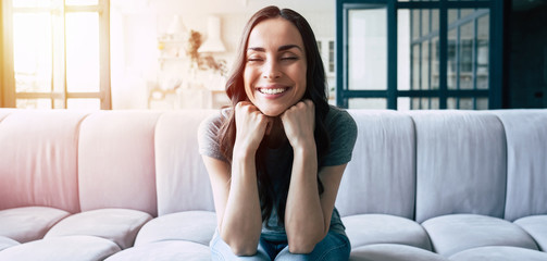 Portrait of smiling happy cute woman with closed eyes sitting on the couch at home
