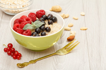 Oatmeal porridge in porcelain bowl with currant berries and raspberries, decorated with mint leaves