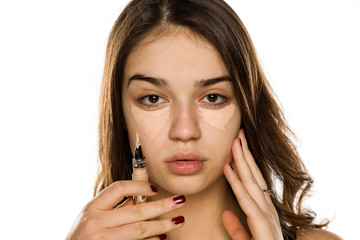 Young beautiful woman applying concealer on white background