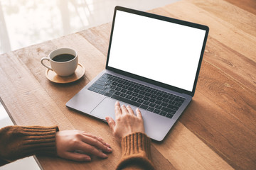 Mockup image of a woman's hand using and touching on laptop touchpad with blank white desktop screen with coffee cup on wooden table - obrazy, fototapety, plakaty
