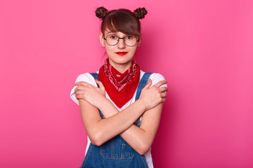 Sincere positive black haired girl standing isolated over pink background in studio, crossing her...