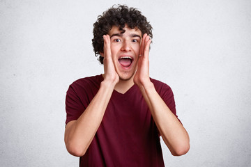 Emotional brunet male has dark curly hair, looks nervously directly at camera, finds someone,...