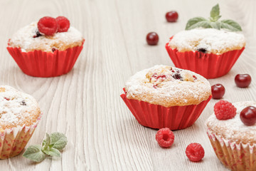 Homemade cupcakes sprinkled with powdered sugar and fresh raspberries and mint.