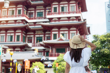 Fototapeta premium Woman traveling with white dress and hat, Asian traveler looking to Buddha Tooth Relic Temple in Chinatown of Singapore. landmark and popular for tourist attractions. Southeast Asia Travel concept