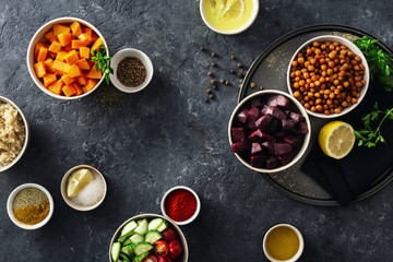 Set of healthy vegetarian ingredients for cooking. Spiced chickpeas, Baked pumpkin and beets, quinoa and vegetables on dark stone background with copy space top view