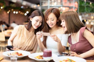 Happy friends having dinner and watching smart phone in  restaurant