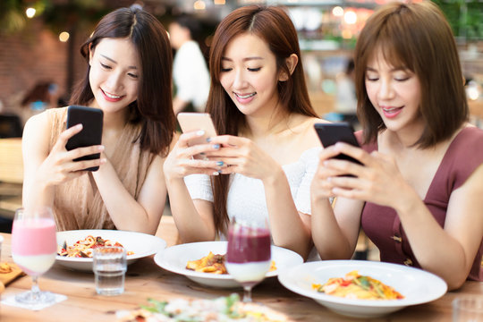 Happy Friends Having Dinner And Watching Smart Phone In  Restaurant