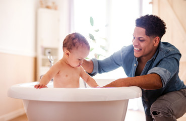 Father washing small toddler son in a bathroom indoors at home.