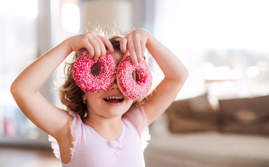 A small girl with doughnuts at home, having fun.