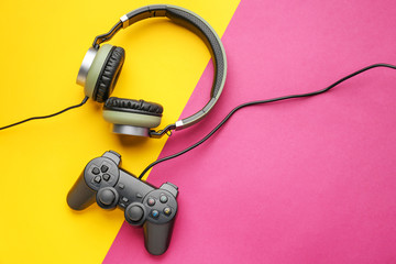 Modern game pad and headphones on color background