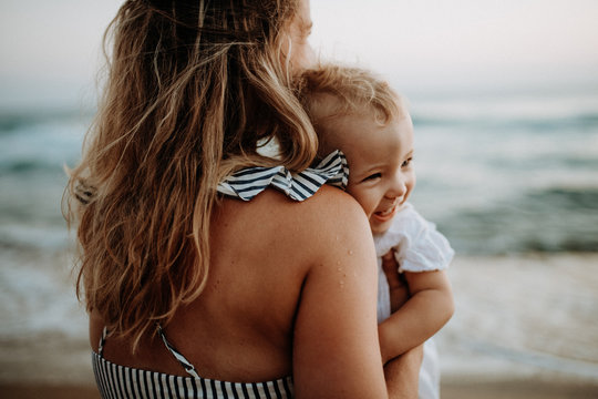 Close-up of young mother with a toddler girl on beach on summer holiday.
