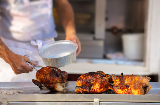 A man takes a roast chicken from the skewer to pack it for the customer in an aluminum jar. A spanish weekly market in nice sunny weather.