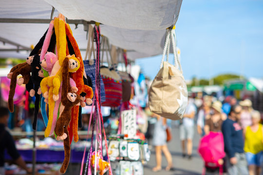 A flea market in Spain with stuffed animals, handbags, monkeys and gifts with many people in the blue sky and sunshine.