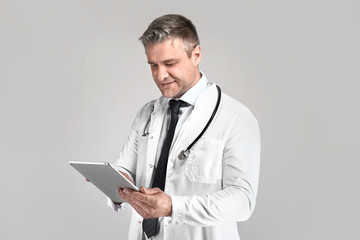 Handsome mature doctor with tablet computer on grey background