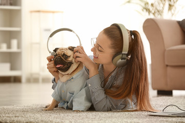 Teenage girl with cute pug dog listening to music at home