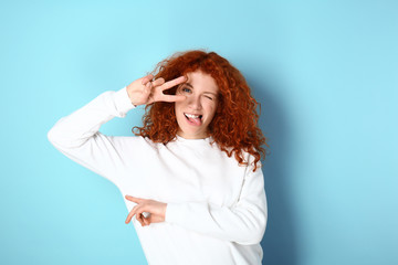 Beautiful redhead woman showing victory gesture on color background
