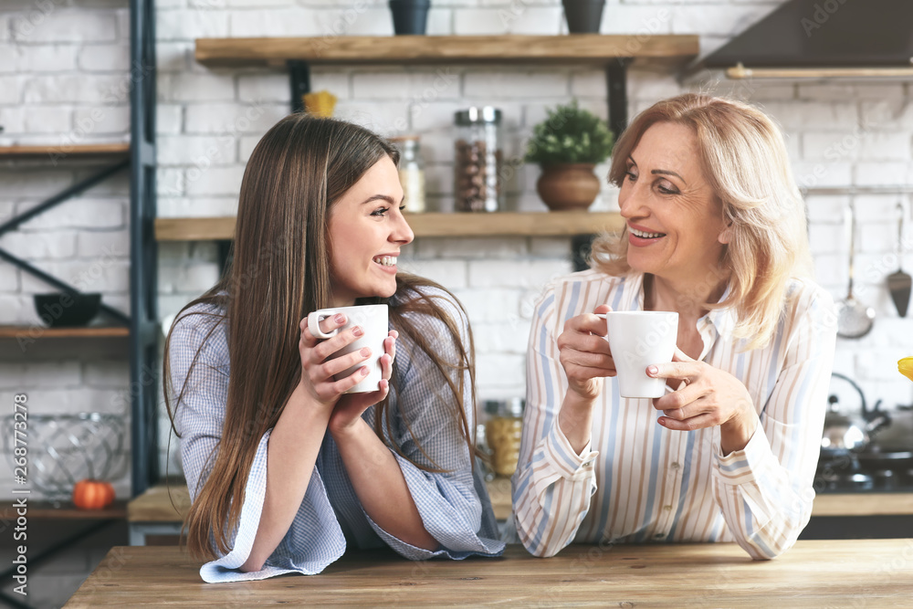 Wall mural happy mother and daughter drinking tea in kitchen at home