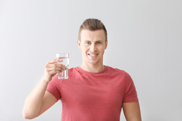 Handsome young man with glass of water on light background