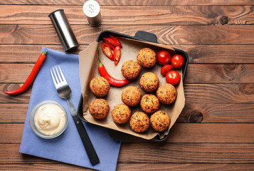 Frying pan with tasty falafel balls and sauce on wooden table