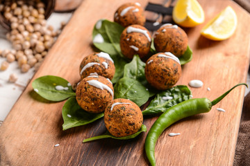 Tasty falafel balls with chili and spinach on wooden board