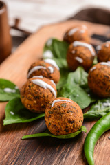 Tasty falafel balls with chili and spinach on wooden board, closeup