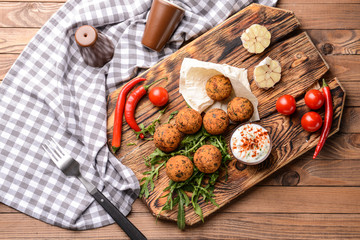 Board with tasty falafel balls and sauce on wooden table
