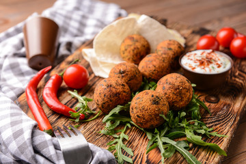 Tasty falafel balls and sauce on wooden board