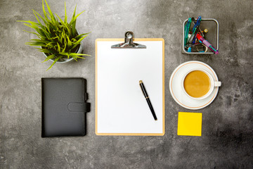 Top view of business desk with potted plant, clipboard, notebook, coffee, notes paper and business accessories