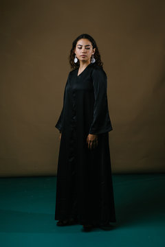  Studio portrait of a beautiful and attractive Malay Asian woman in a traditional black baju kurung dress against a brown background. She has frizzy beautiful hair and is posing for her portrait. 