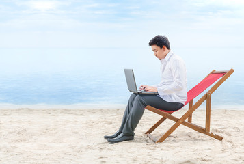 Asian businessman working with laptop sitting in the beach chair on beach