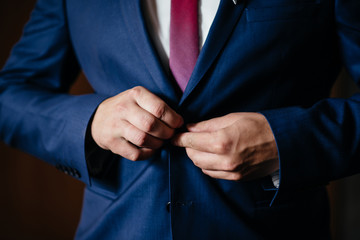 Portrait of serious handsome man in blue suit and tie buttoning jacket