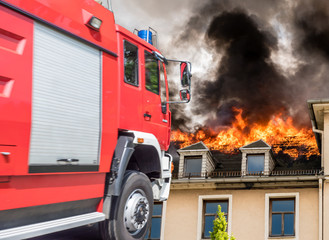 Feuerwehreinsatz mit brennenden Haus im Hintergrund