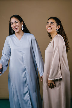 Portrait of two young Middle Eastern Muslim women smiling as they pose for their photo. They are wearing traditional pastel coloured Baju Kurung dresses to visit during Raya.