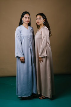 Portrait of two young Middle Eastern Muslim women as they pose for their photo. They are wearing traditional pastel coloured Baju Kurung dresses to visit during Raya and both have neutral expressions.