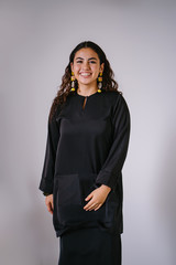 Studio portrait of a beautiful, young and attractive Malay Asian woman in a traditional black baju kurung dress for Raya (Eid). She is smiling as she gazes at the camera against a white background.  M