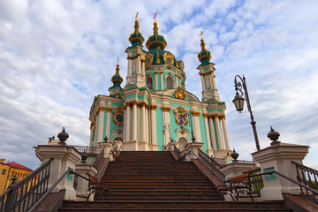 Fototapeta na wymiar Metal stairs with beautiful lanterns to the Saint Andrew's Church. Famous touristic place and travel destination in Kyiv, Ukraine. Cathedral against cloudy sky. Spring morning view