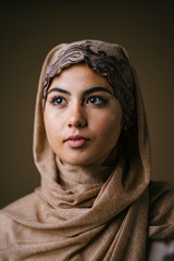 Portrait head shot of a young and beautiful Muslim Middle Eastern woman in a brown traditional...