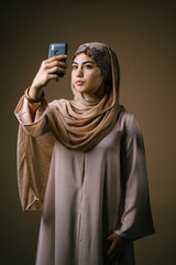 A young and beautiful Muslim woman in a traditional outfit and hijab head scarf is looking at her...